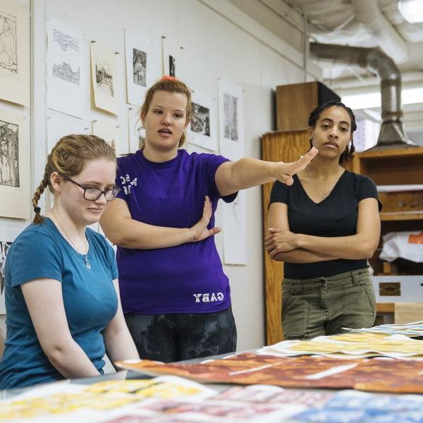 Three Agnes Scott studio art major students observe pieces of art in class.