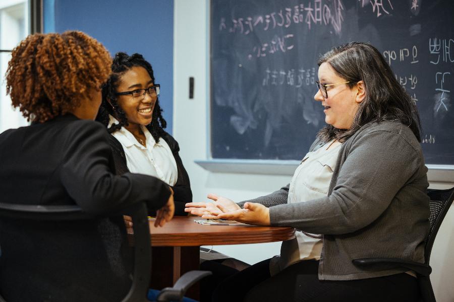 three adults sit at a round table in a classroom having a jovial discussion